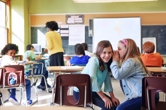 Happy, children and whisper secret in classroom for rumor story, gossip together or lesson. Learning, friends or girl students with private chat in ear at school for mystery news or sneaky discussion