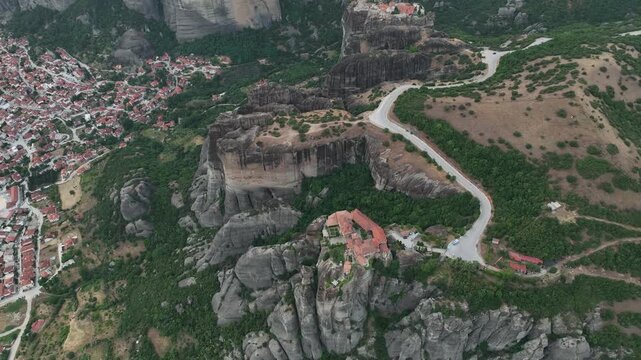 Aerial view of monasteries perched atop towering rock formations, a winding road snakes through the landscape, Meteora, Greece.