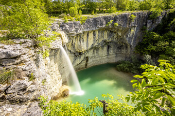 View of a cascading waterfall plunges into a vibrant turquoise pool surrounded by rugged cliffs and lush greenery, Kotli, Istria County, Croatia.