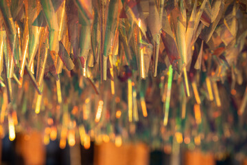 Warm festive abstract background of shimmering metallic tinsel with golden, iridescent glowing. Celebration, festive magic, winter holidays, elegant decor. Sparkling holographic foil decoration.