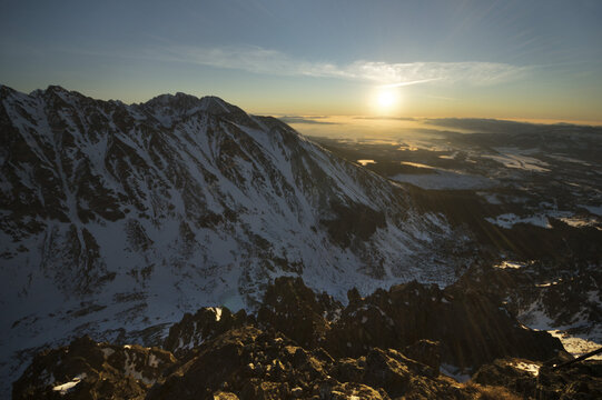 View of snow-capped mountains rise majestically against a backdrop of the setting sun in a serene winter landscape, Vysoke Tatry, Presovsky kraj, Slovakia.