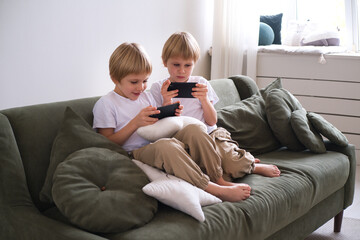 kids boys twins using smartphones on the couch in living room