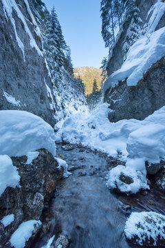 View of icy river cascading through a snowy gorge, flanked by towering cliffs, under a clear sky in winter, Prosiek, Zilinsky kraj, Slovakia.