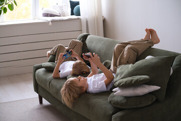 kids boys twins using smartphones lying on the couch
