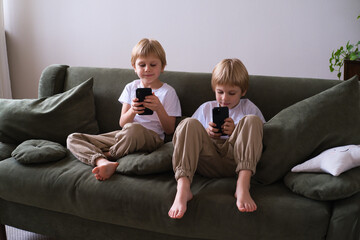 kids blonde boys twins using smartphones on the couch in living room