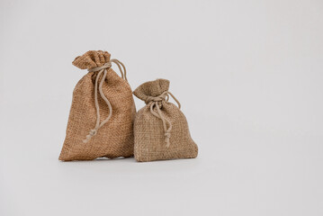 Two burlap sacks of different sizes are placed on a white background. The larger sack is brown,...