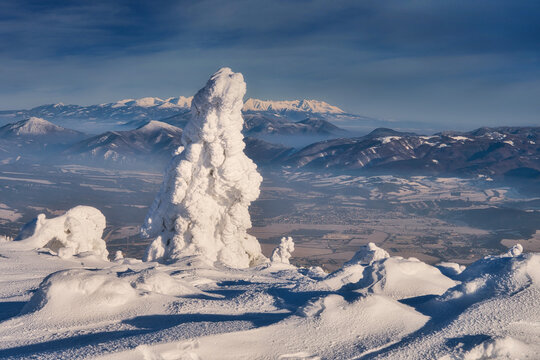 View of snow-laden landscape with a striking, frost-covered rock formation standing tall against a backdrop of distant, hazy mountains, Mala Fatra, Zilina Region, Slovakia.