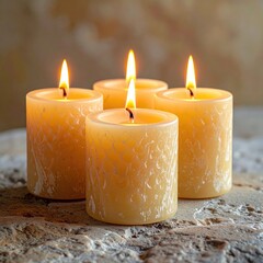 Four lit candles, pale yellow, textured, on a stone surface