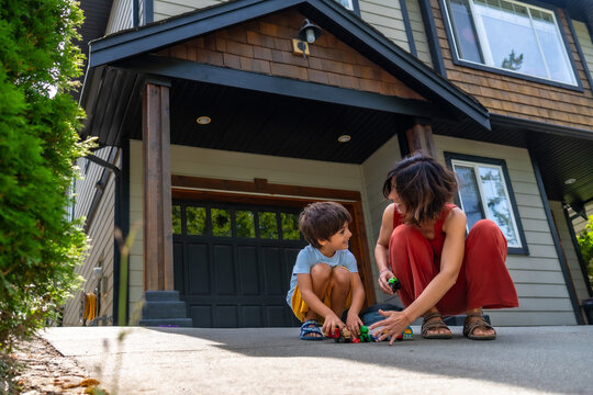 Mother and son playing with toy cars in front of house