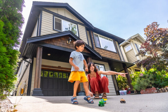 Mother and son playing with toy cars in front of house