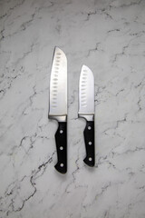 A pair of metal knives with black handles of excellent quality on a gray marble table. Tools, edged weapons, hobbies, hunting.