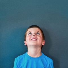 Obraz premium Excited, happy and child looking up in studio for omg news, opinion and feedback on blue background. Mockup space, surprise and face of isolated young boy with announcement, information and deal