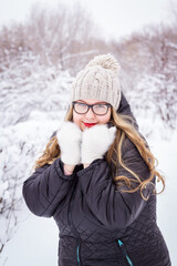 Fototapeta premium Happy plus size woman in glasses and white mittens posing in snowy winter park