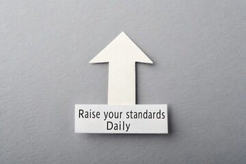 White Upward Arrow Symbol with 'Raise your standards Daily' Text on a Gray Background