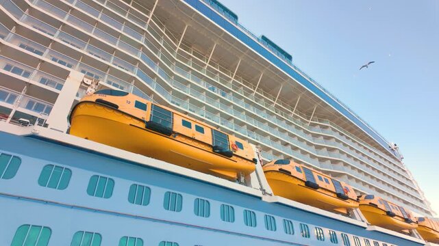 Large cruise ship with multiple life boats on a sunny day, showcasing modern maritime design and safety features