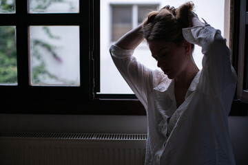 Portrait of woman in silhouette by window in darkness