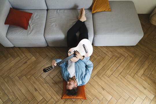 Young man playing acoustic guitar on cozy floor