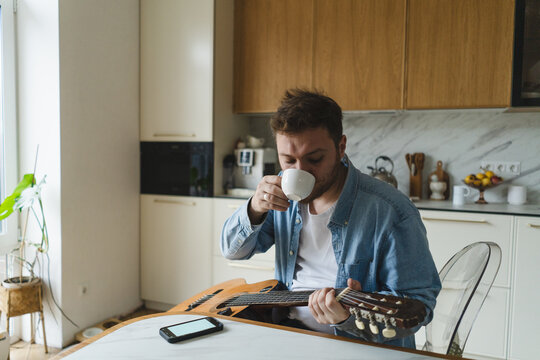 Young man enjoying music at home with guitar