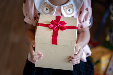 Child Holding a Large Beige Gift Box with Bold Red Ribbon Bow for Christmas or Holiday Giving