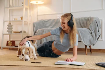 Fotobehang Ridders In headphones, listens to the music, with animal. Happy girl is on the floor at home with dog, domestic room  © standret