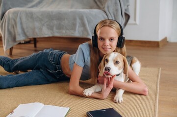 Looking forward, in headphones, embracing animal. Happy girl is on the floor at home with dog, domestic room