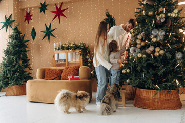 By the decorated tree. Happy family with child and dog celebrating Christmas together at home