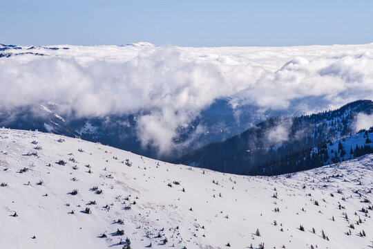 Aerial view of a serene snow-covered Kosarisko, framed by a cloud inversion against the distant mountain peaks, Nizke Tatry, Banska Bystrica region, Slovakia.