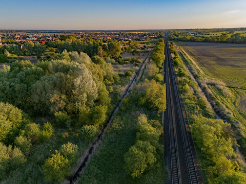 Aerial view of railway tracks cutting through a vibrant tapestry of green trees and fields near the village, Zohor, Bratislava Region, Slovakia.