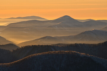 Aerial view of majestic mountains bathed in the warm glow of the sunset, casting long shadows across the snow-dusted peaks, Vidlica, Zilina Region, Slovakia.