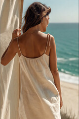 Woman in light summer dress standing by seaside window with ocean view