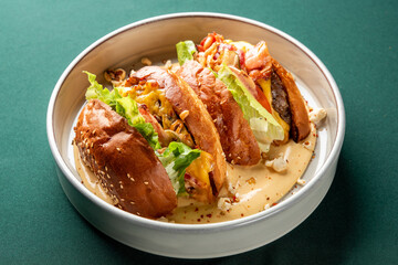 A close-up shot of several mini burgers, or sliders, served in a bowl with rich cheese sauce, lettuce, and a sprinkle of popcorn