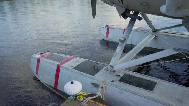 Detail of seaplane float and struts touching still lake surface in remote boreal setting, tied to cleat on piertie