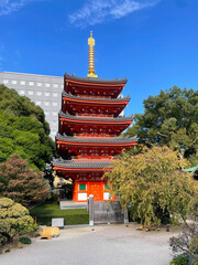 Vibrant red pagoda and ornate temple roof with palm trees and blue sky, representing traditional Japanese architecture.