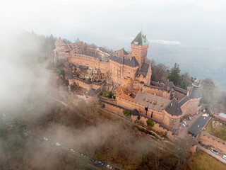 High-angle close-up side view of Ch&acirc;teau du Haut-Koenigsbourg enveloped in clouds, highlighting the fortress walls, towers, and dramatic elevated setting in Alsace.

