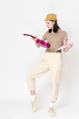 Young female ukulelist holding ukulele and sheet music, studying chords. Full length view of 18 year old woman of Caucasian ethnicity wearing straw hat, brown t-shirt, light jeans and sneakers