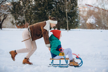 Mother pushing son on sled in winter park