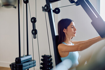 Young woman training using weights on a multi-station gym machine. Practicing strength fitness...