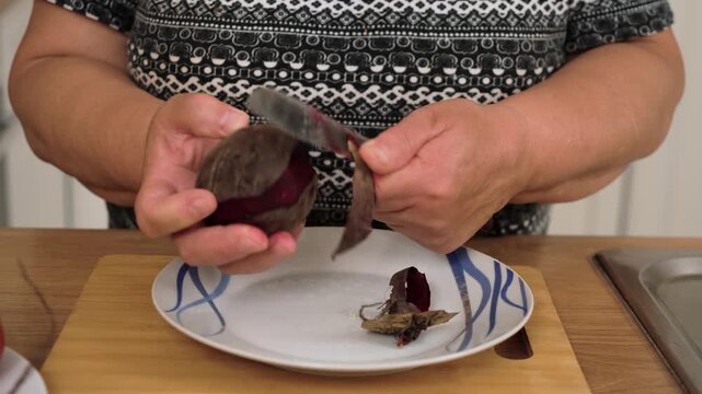 Peeling beetroot for cooking traditional Ukrainian borscht. Removing beet skin preparing ingredients for national soup of Ukraine. Trimming boiled root setting up components for classic Slavic dish