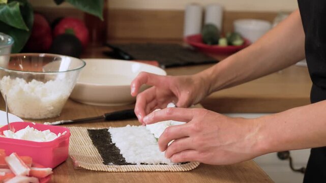 Adding cream cheese on cucumber and crab stick over rice. Unrecognizable person layering sushi roll filling. Placing soft cheese topping inside sushi base. Preparing rich filling before rolling sushi