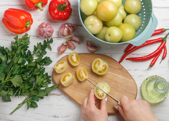 A woman prepares a spicy savory snack made from fresh vegetables - green tomatoes, red bell pepper, hot chili pepper, garlic, parsley and spices. White wooden table