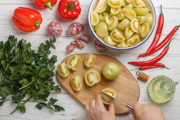 A woman prepares a spicy savory snack made from fresh vegetables - green tomatoes, red bell pepper, hot chili pepper, garlic, parsley and spices. White wooden table
