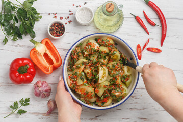 A woman prepares a spicy savory snack made from fresh vegetables - green tomatoes, red bell pepper, hot chili pepper, garlic, parsley and spices. White wooden table