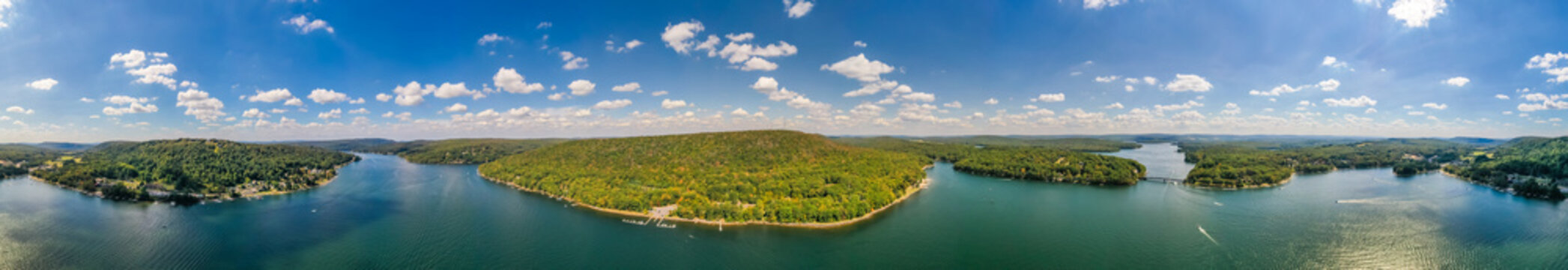 Aerial view of Deep Creek Lake's shimmering waters winding around lush green peninsulas under a bright blue sky dotted with fluffy white clouds, Deep Dreek, Maryland, USA.