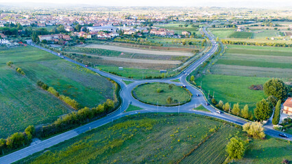 Aerial view of the roundabout amidst a landscape of vibrant green fields and distant buildings, a tapestry of rural charm, Siena, Tuscany, Italy.