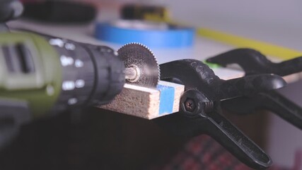 Close-up of a worker cutting a clamped wooden board with a rotary tool in a workshop
