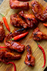 Close up of spicy glazed chicken wings with red chili peppers on rustic wooden board. Detailed food texture image ideal for spicy food concepts, barbecue meals, comfort food, and culinary backgrounds