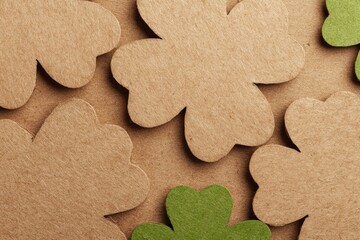 Fototapeta premium Shamrock-shaped brown and green paper cutouts arranged on a brown craft paper background creating a simple and textured visual pattern with overlapping shapes and natural tones