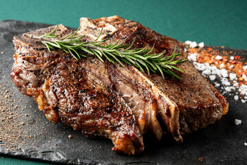 Juicy grilled T-bone beef steak seasoned with salt, pepper, and rosemary on a black stone serving board, viewed from above