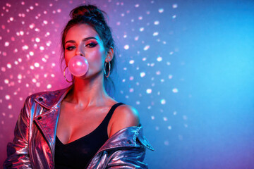 Young woman blowing pink bubble gum bubble with shiny metallic jacket