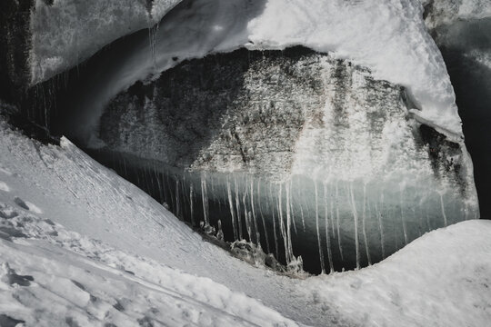 View of frozen icicles hanging from a snowy overhang with a ground perspective in the cold, Morteratsch Glacier, Pontresina, Grisons Canton, Switzerland.